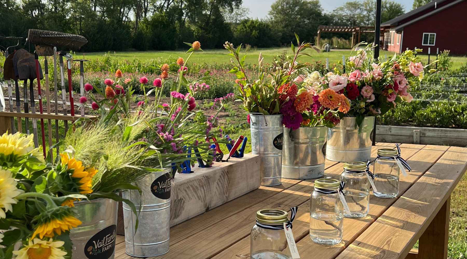 Flowers of different varieties in galvanized buckets on a wooden table with empty jars nearby for arranging bouquets.