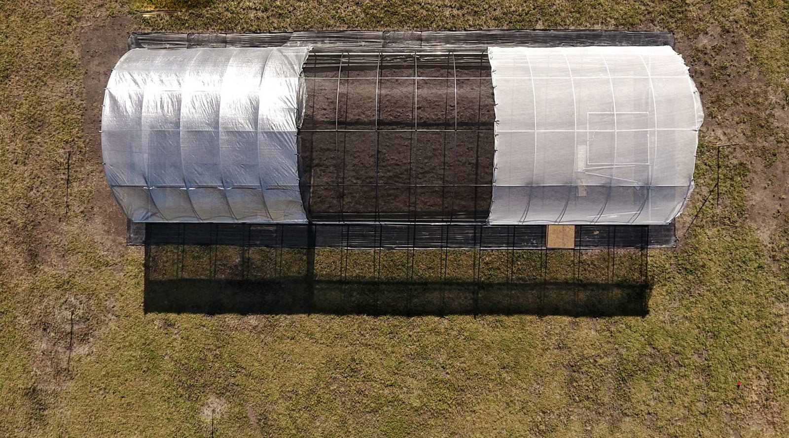 The top of a high tunnel covered with three different colors of shade cloth; aluminum, black, and white shade sloth are casting shadows in the foreground.