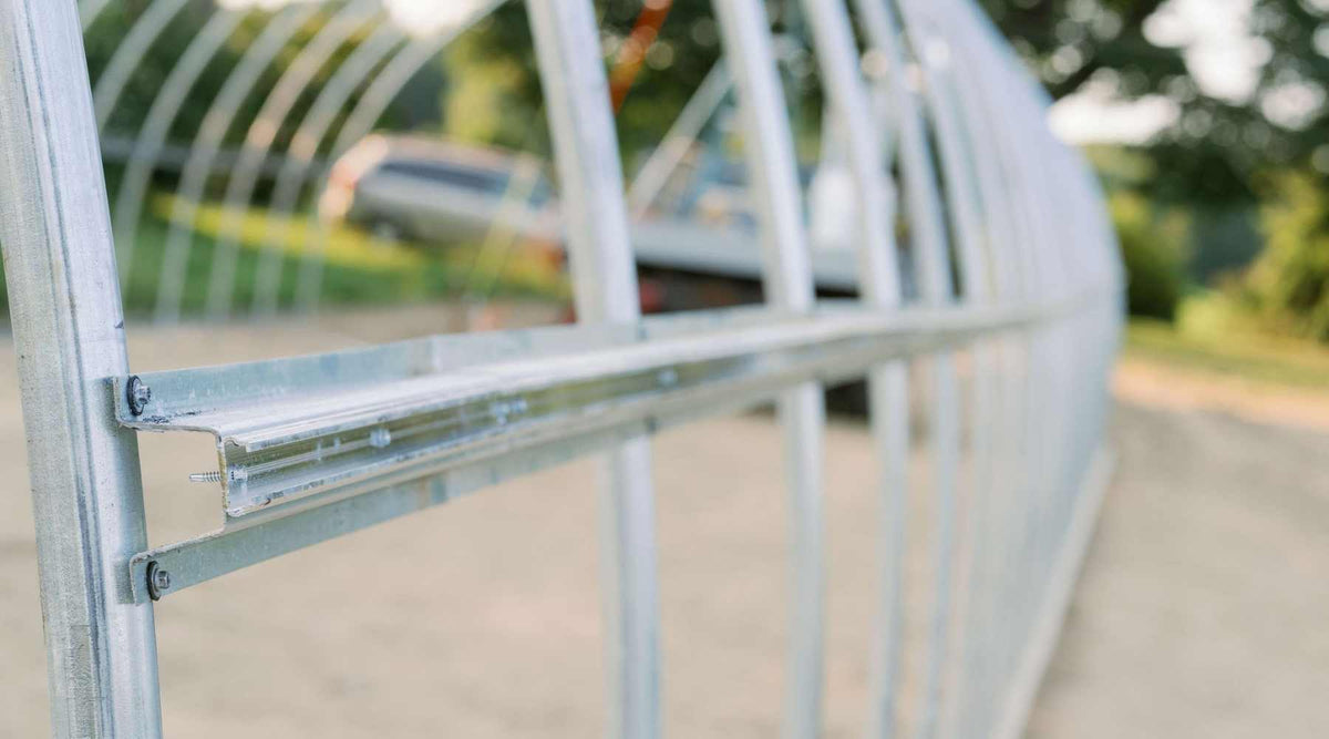 Close-up of a hoop house structure under construction with metal framing in an outdoor setting.