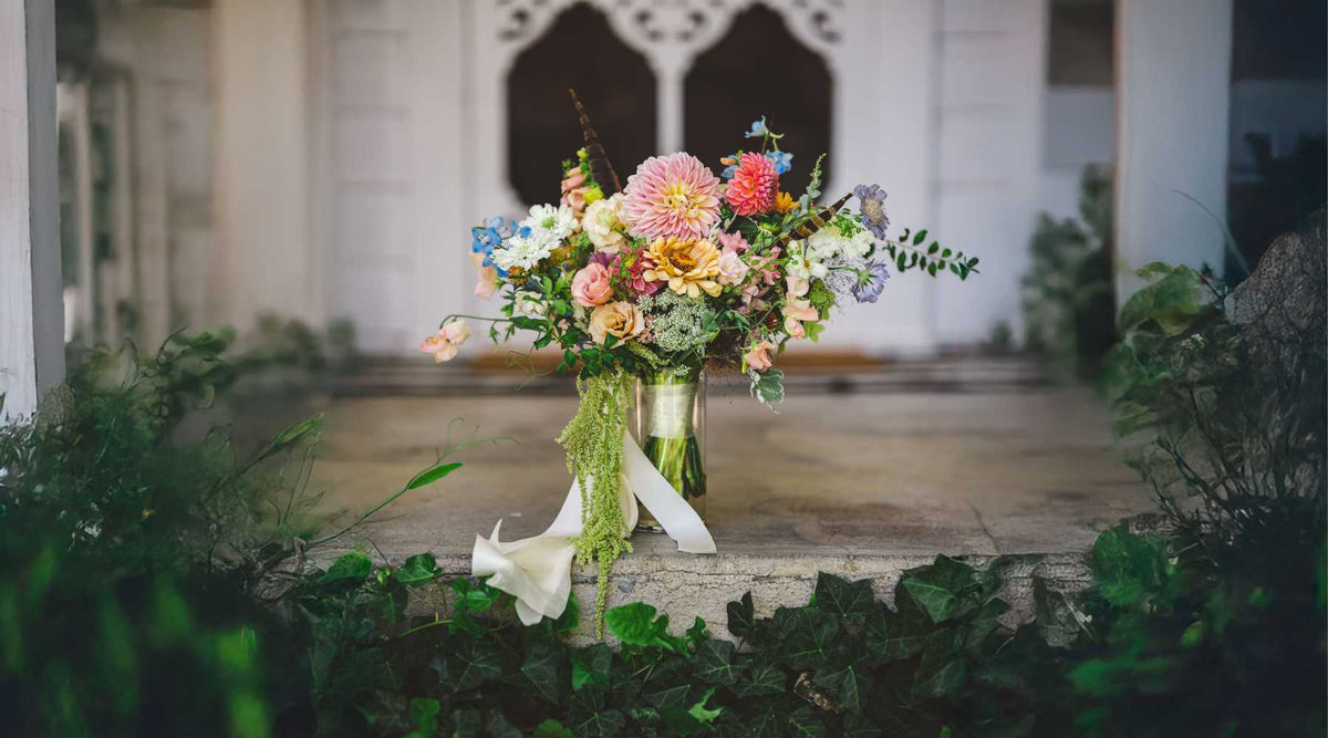 A lush, seasonal bridal bouquet with a mix of focal and filler flowers—peonies, dahlias, lisianthus, etc.—held or displayed in soft natural light.