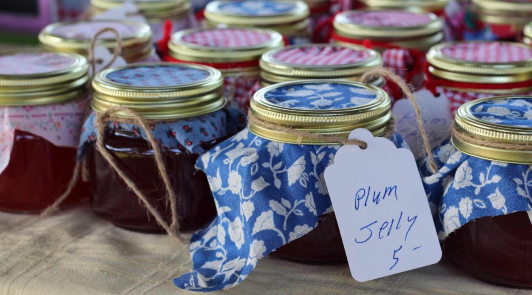 Jars of homemade plum jelly with varied fabric squares over the lids. 
