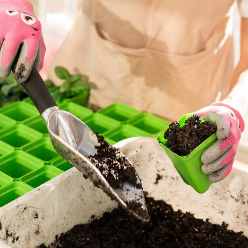 Boy filling green seed starting pot with soil with tool