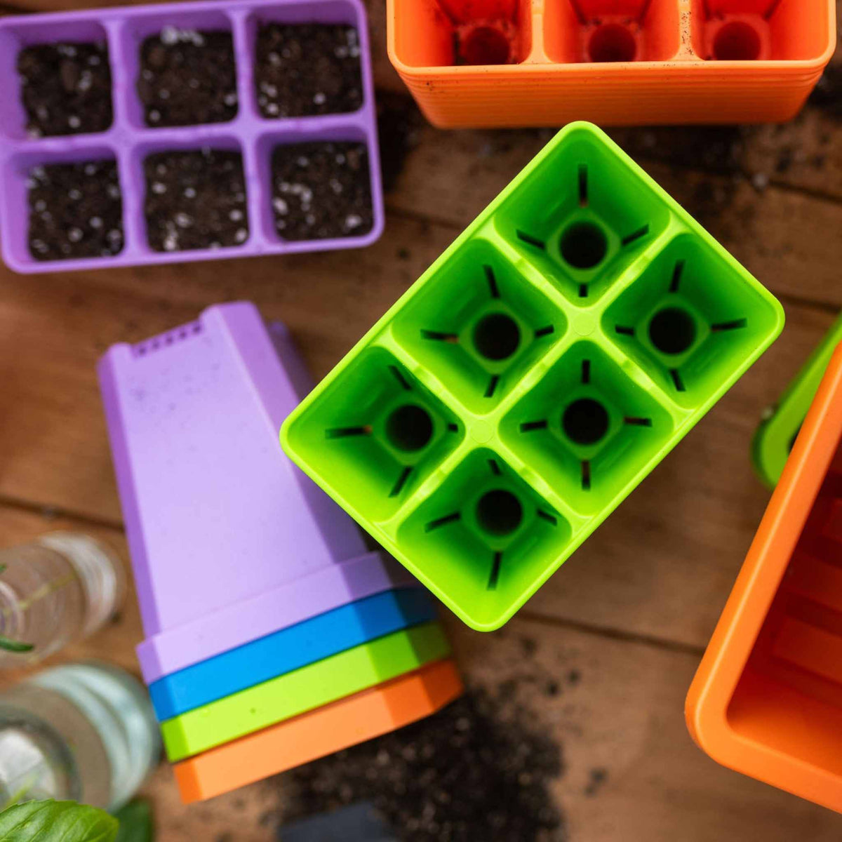 Stack of 3.3" Seed starting pots in purple, blue, green, and orange next to partially filled 6 cells in orange, green and purple.