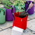 Using a shovel to plant in red grow bag with purple and green grow bags in the background